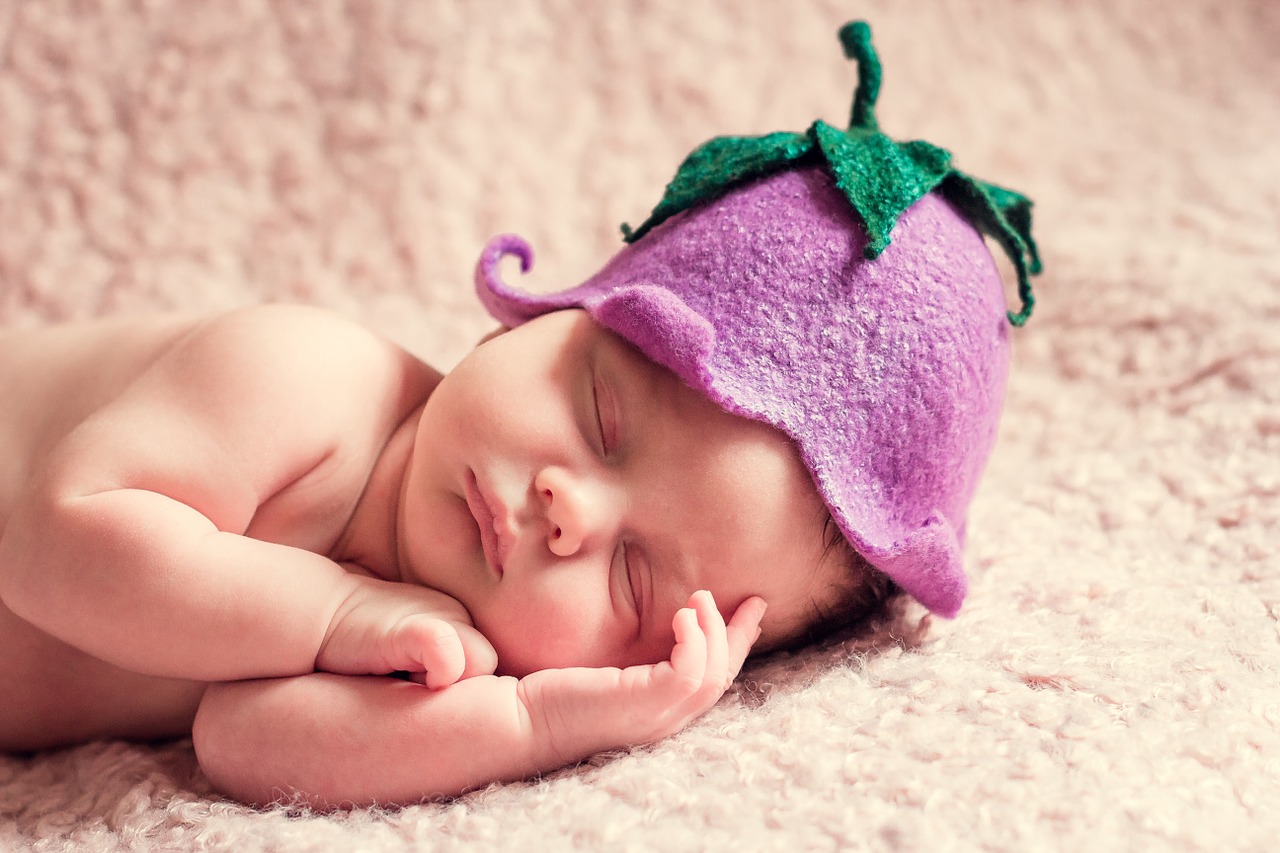 Baby mit Hütchen liegt schlafend auf der Seite
